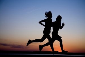 Young couple: man and woman run together on a sunset on lake coast. Silhouette.